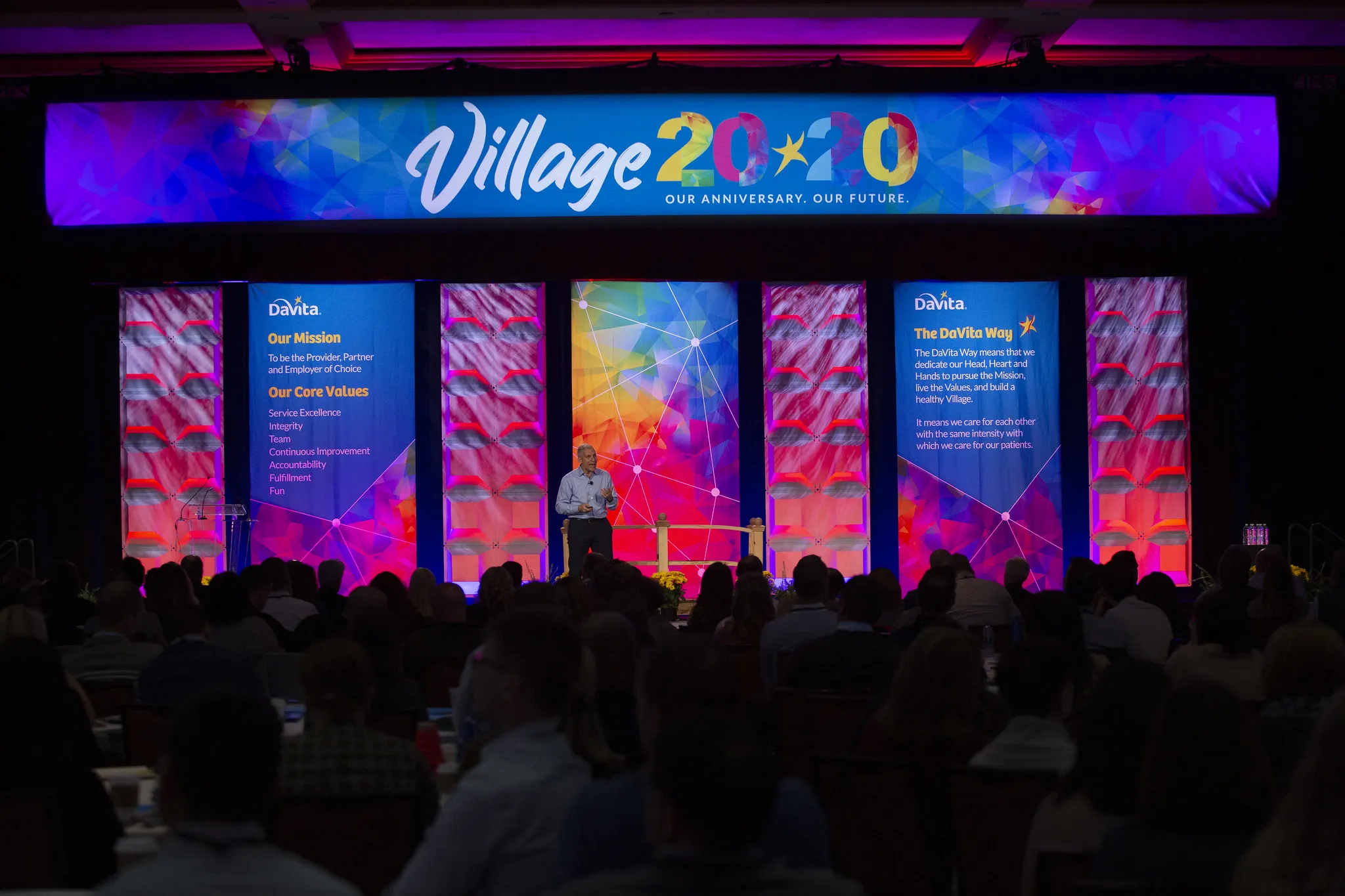 Business conference featuring vibrant backlit hanging banners on the stage.