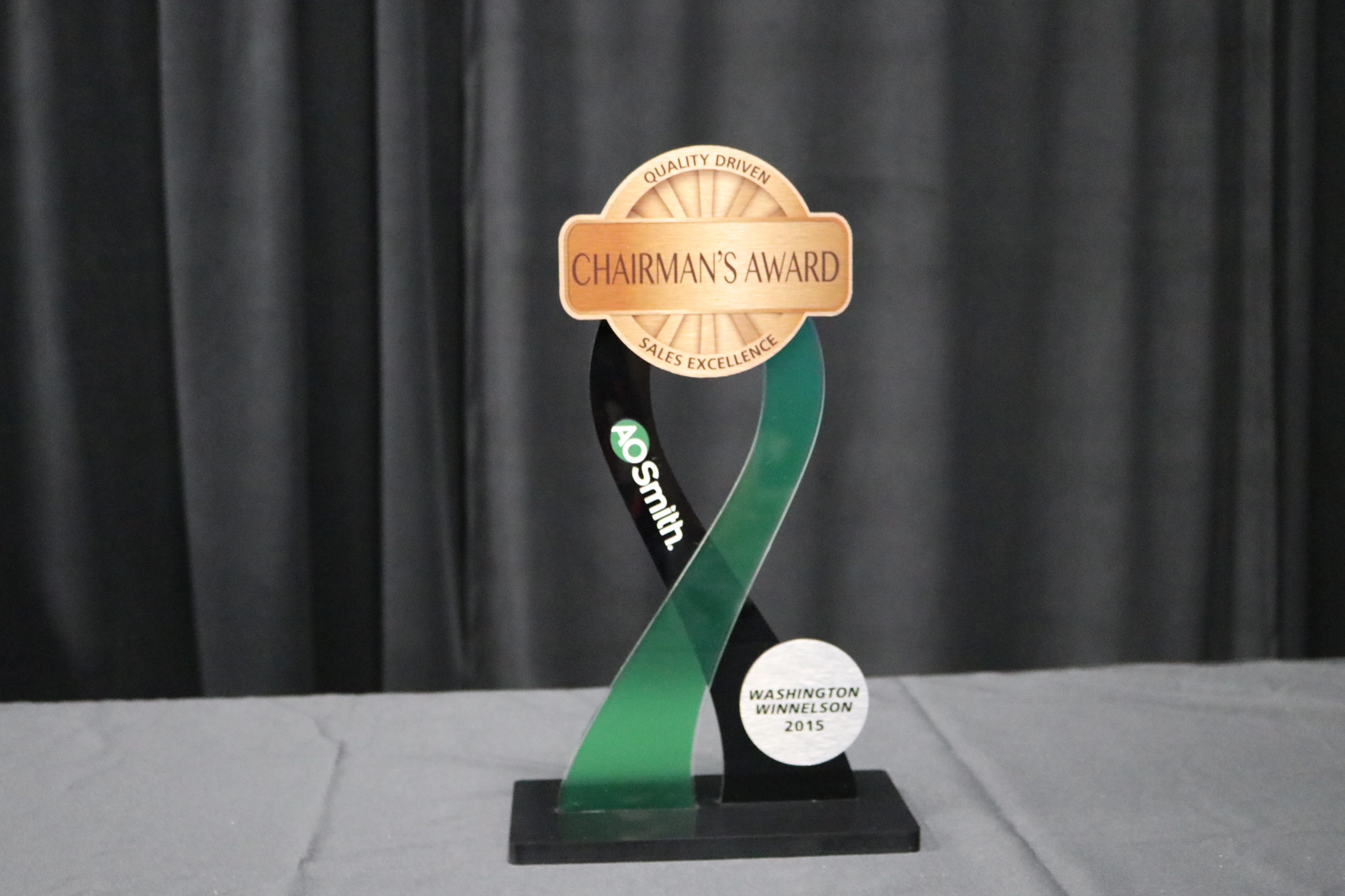 Acrylic tabletop award with black and frosted acrylic ribbons meeting at a brushed bronze center piece.