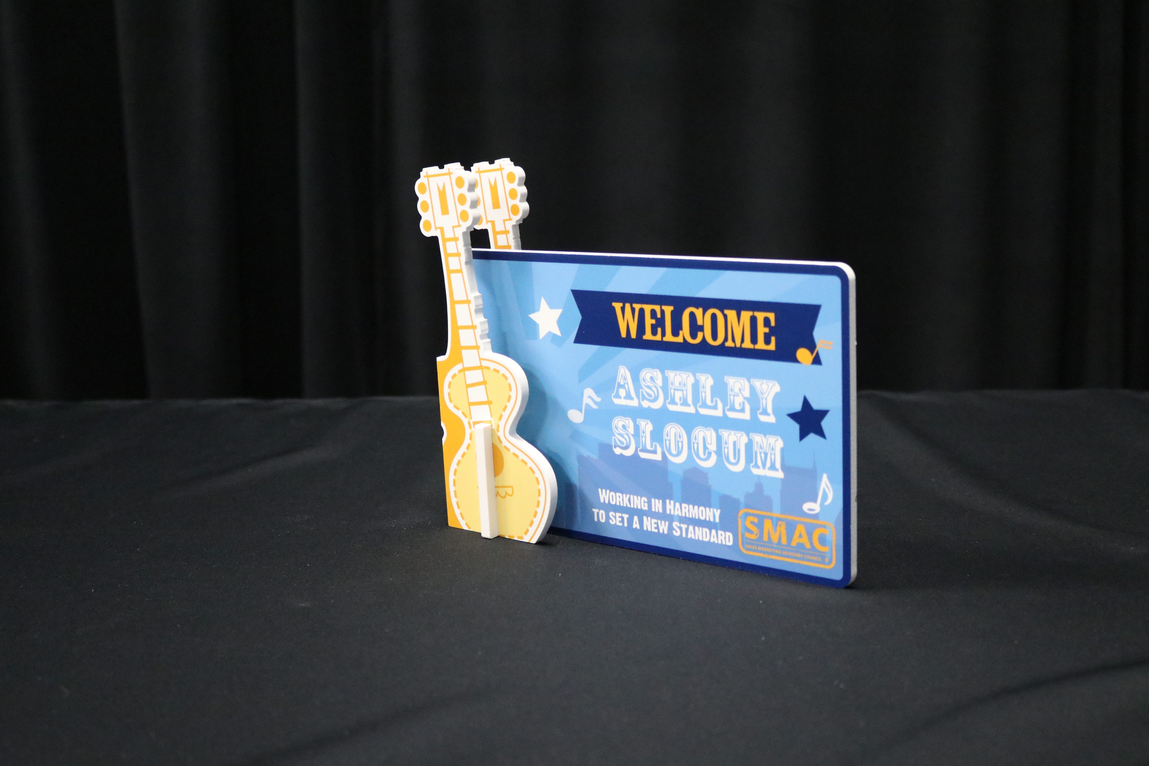 Convention tabletop display with 3D guitars cut out holding sign welcoming teammate.