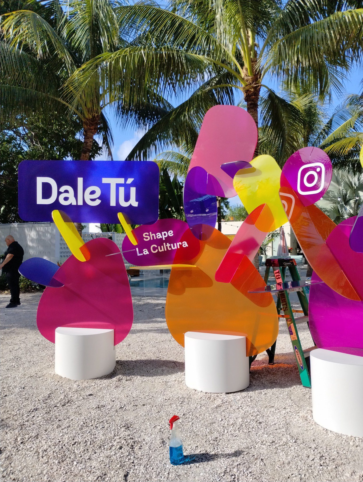 A free-standing acrylic display with colorful printing on clear acrylic, placed on a beach.