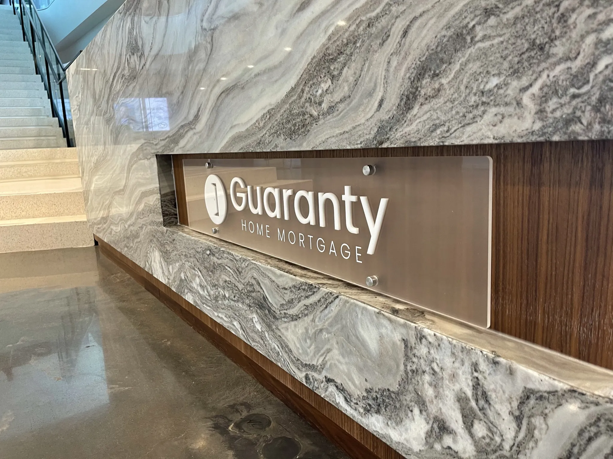 Lobby logo displayed on a frosted acrylic panel with white 3D letters mounted using silver stand-offs on a desk.